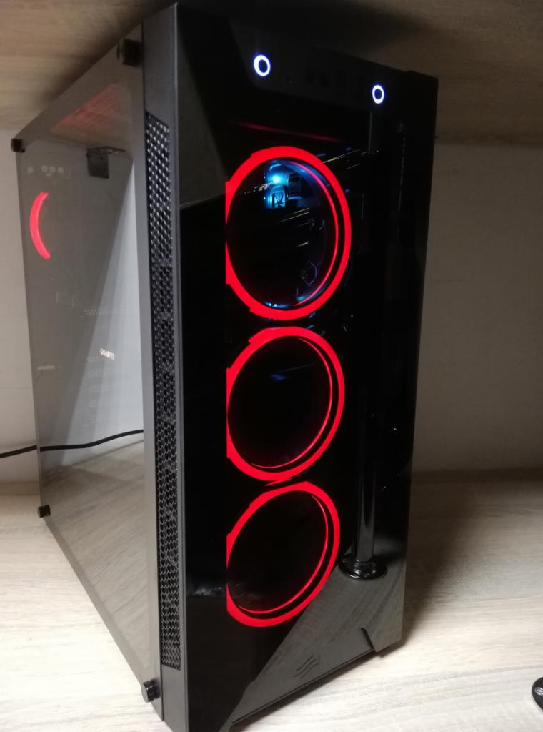 Czarna obudowa komputera stacjonarnego z przeszklonym bokiem, podświetlana trzema czerwonymi wentylatorami i dwoma niebieskimi diodami na górze, stojąca na drewnianym blacie.