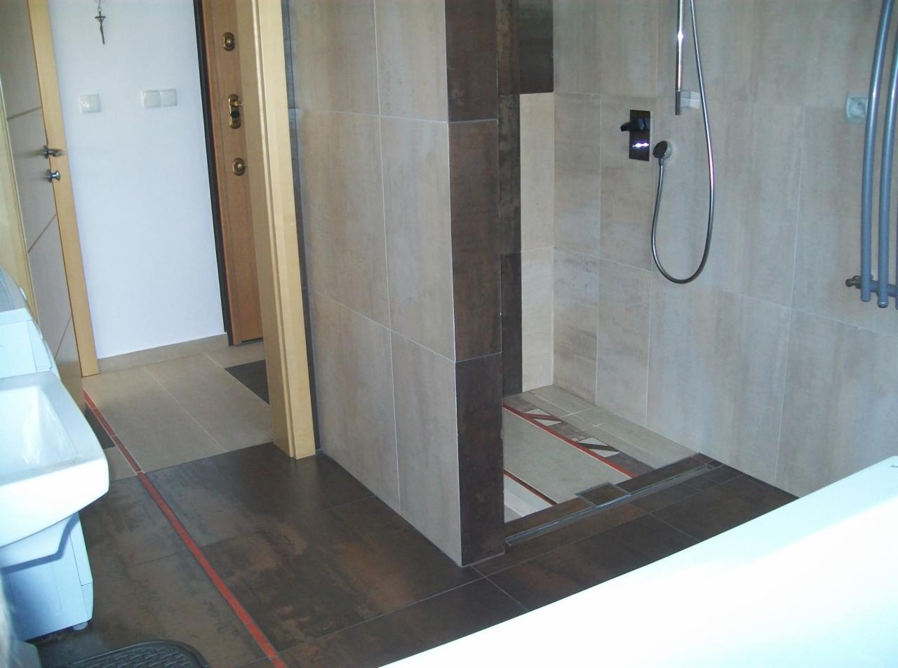 Nowoczesna łazienka z kabiną prysznicową typu walk-in, wykończona płytkami w odcieniach beżu i brązu, z widocznym odpływem liniowym i elementami armatury.