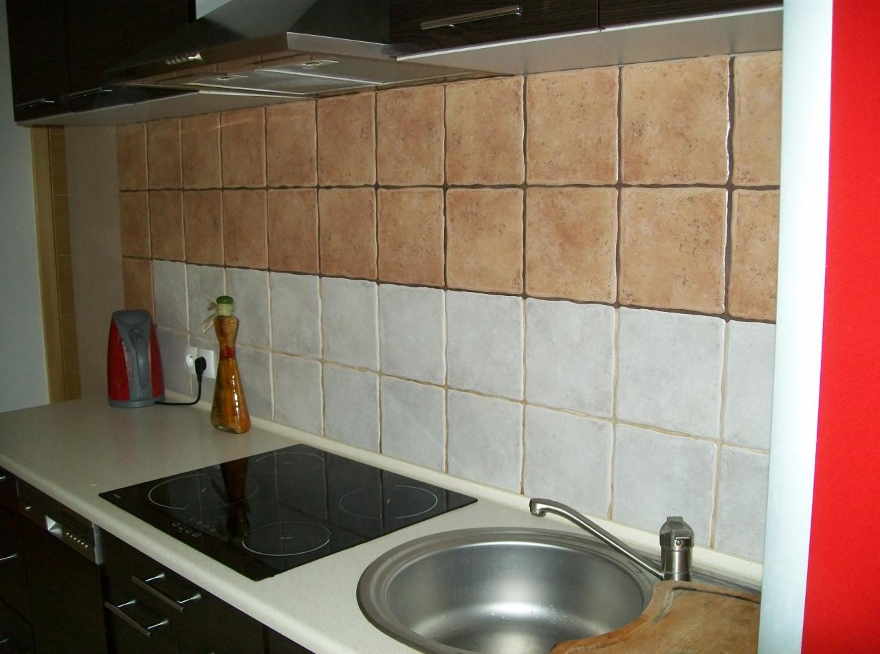 Kuchnia z dwukolorowymi, kwadratowymi płytkami na ścianie nad blatem, brązowymi u góry i białymi na dole, z widocznym zlewem, płytą grzewczą i elementami wyposażenia.