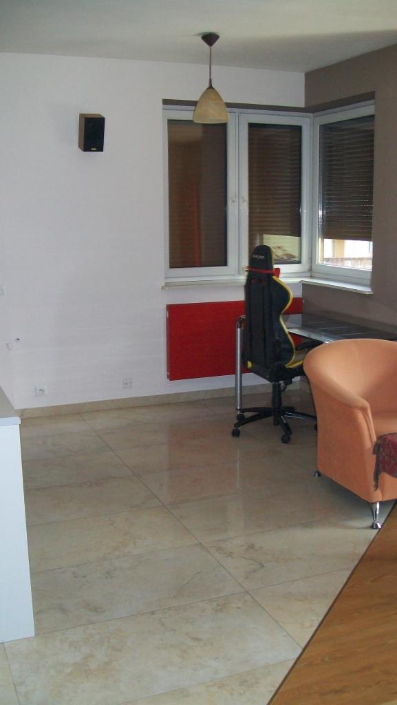 Beżowa podłoga z płytek ceramicznych w pokoju z czerwonym grzejnikiem, biurkiem i fotelem gamingowym.