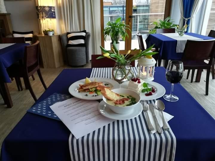 Elegancko zastawiony stół w Olsztynie z zupą krem, rybą, deserem i winem, udekorowany kwiatami i lampionem, w marynistycznym stylu.