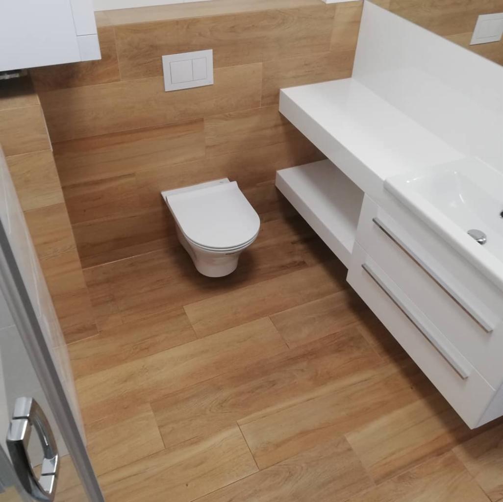 Nowoczesna łazienka z toaletą wiszącą, umywalką na białym blacie i brązowymi płytkami imitującymi drewno na ścianach i podłodze, widok z góry.