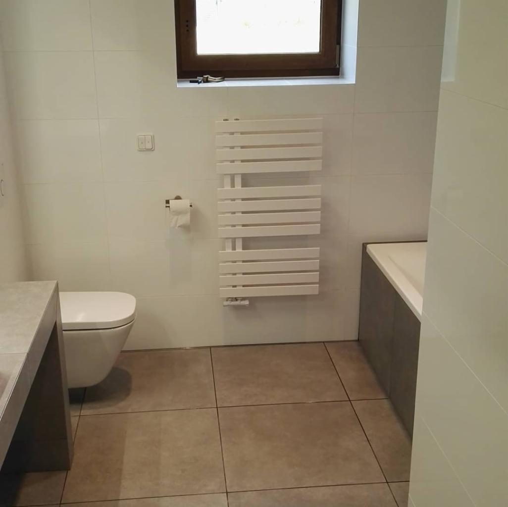 Nowoczesna łazienka z beżowymi płytkami podłogowymi, białymi płytkami ściennymi, grzejnikiem drabinkowym i podwieszaną toaletą.