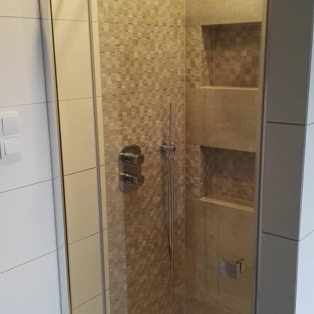 Wykończona kabina prysznicowa z mozaiką w odcieniach beżu i brązu, widoczne wnęki na kosmetyki i nowoczesna armatura.