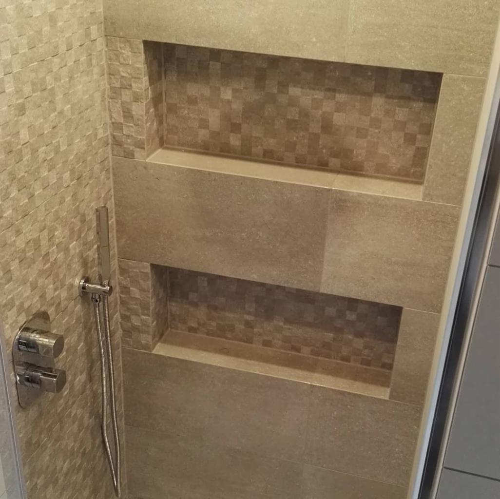 Beżowa kabina prysznicowa z wnękami wykończonymi mozaiką i baterią podtynkową z deszczownicą.