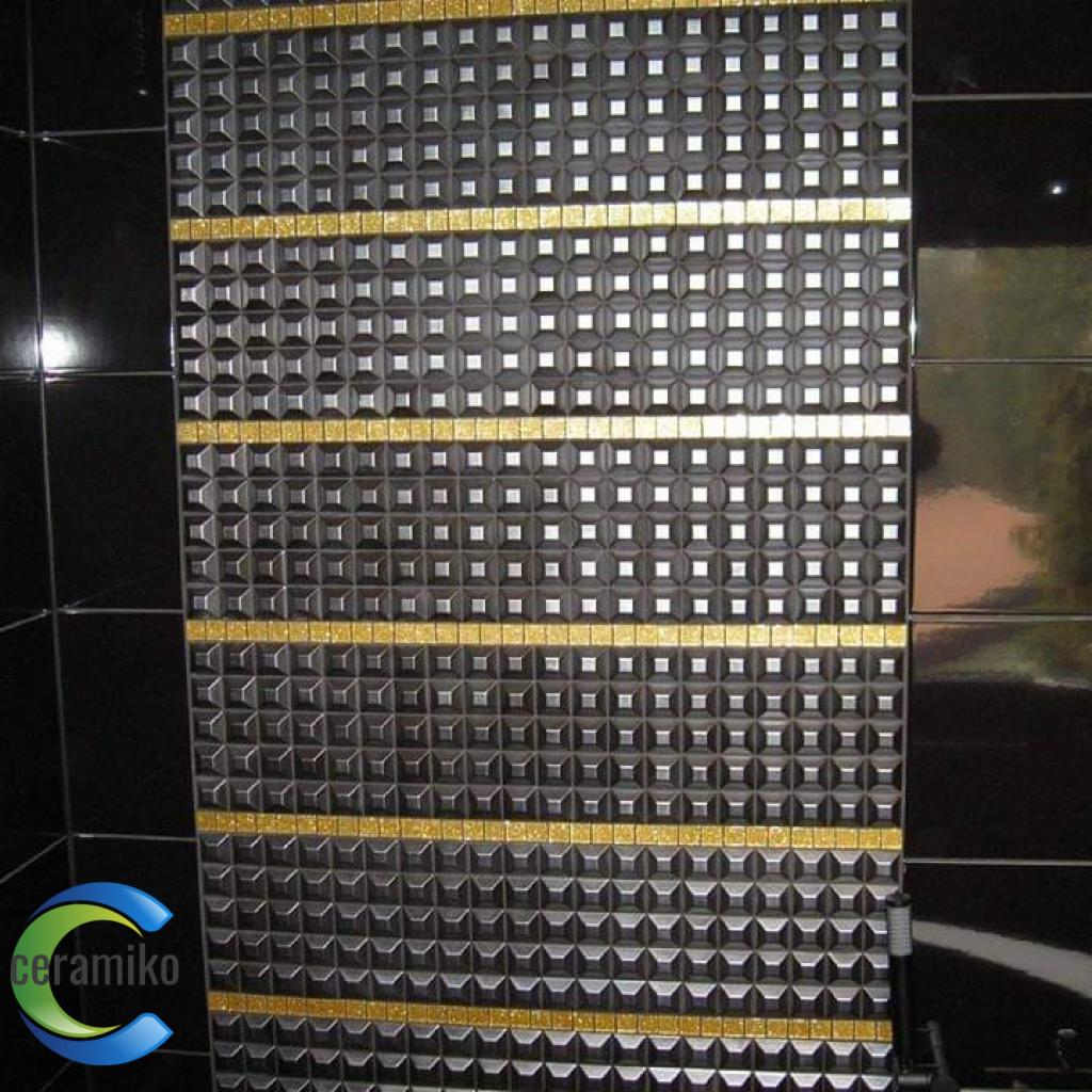 Część ściany wyłożona czarną, błyszczącą mozaiką z wypukłymi kwadratami, przedzielona złotymi pasami. Obok widoczne czarne, duże płytki.
