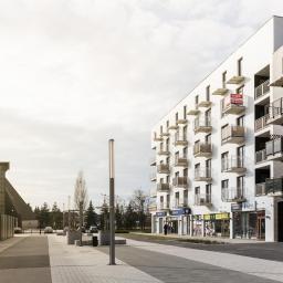 Salon Kosmetyczny FOR YOU Agnieszka Dudek - Nowoczesny budynek apartamentowy z balkonami i lokalami usługowymi na parterze, widok z poziomu chodnika w słoneczny dzień, w tle kościół.