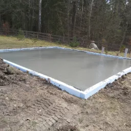 Wylany fundament z izolacją pionową z XPS, widoczna łopata wbita w ziemię i otaczający las.