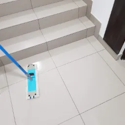 Białe płytki podłogowe i schody czyszczone płaskim mopem z niebieskim uchwytem.