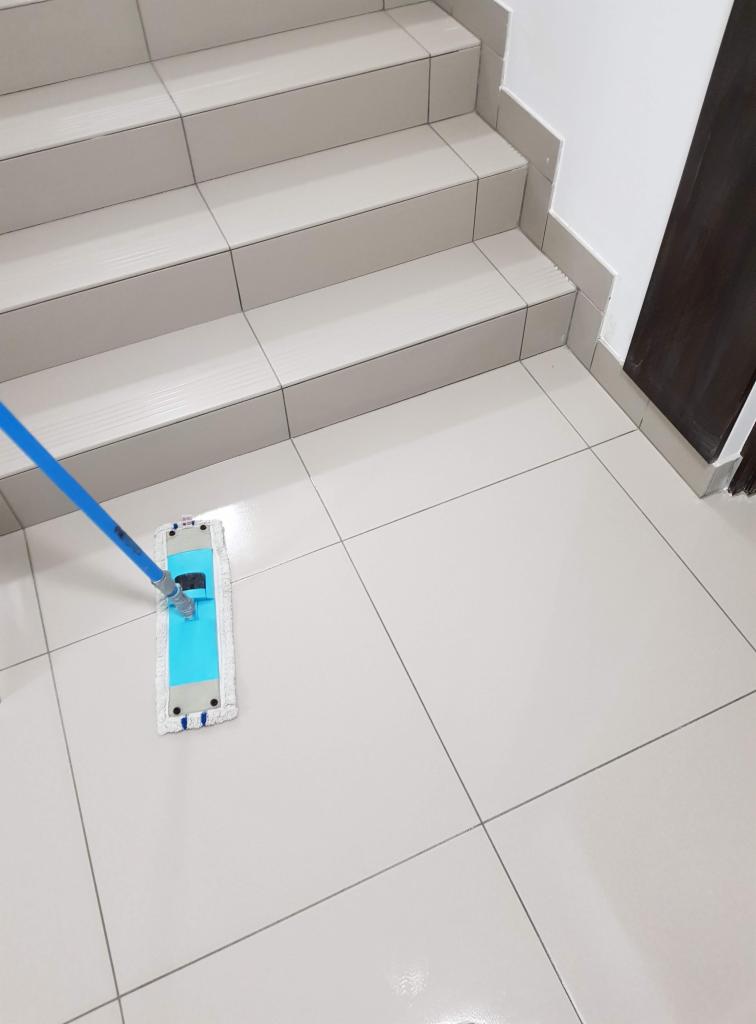 Białe płytki podłogowe i schody czyszczone płaskim mopem z niebieskim uchwytem.