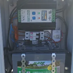 Wnętrze skrzynki z akumulatorem Haze, kontrolerem hybrydowym wiatrowo-solarnym i bezpiecznikami, okablowanie w białej obudowie.