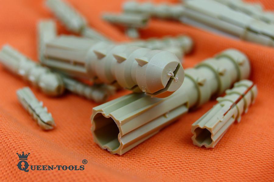 Zbliżenie na zestaw kołków rozporowych z tworzywa sztucznego na pomarańczowym tle, z widocznymi detalami konstrukcji i logo producenta Queen-Tools w lewym dolnym rogu.