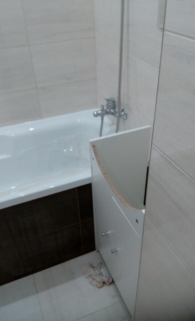 Biała wanna z obudową w trakcie montażu; widoczne niedokładne spasowanie frontu szafki, chromowana bateria i szara płytka ścienna.