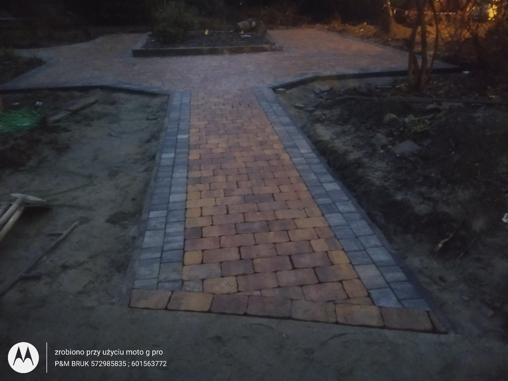 Świeżo ułożony chodnik z kostki brukowej w odcieniach pomarańczy i szarości, z widocznymi narzędziami brukarskimi w tle i ziemią po bokach, wykonany w kształcie gwiazdy.