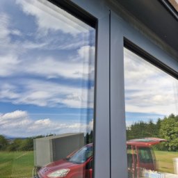 Eko-Błysk - Widok przez czyste okno na czerwony samochód dostawczy, sprzęt do czyszczenia i krajobraz z błękitnym niebem i chmurami.