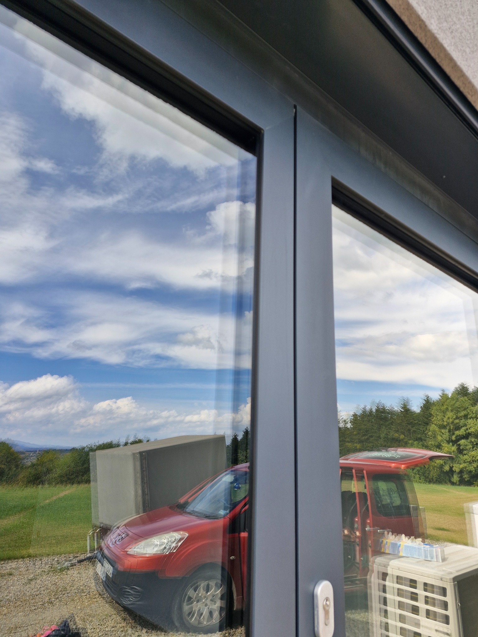 Widok przez czyste okno na czerwony samochód dostawczy, sprzęt do czyszczenia i krajobraz z błękitnym niebem i chmurami.