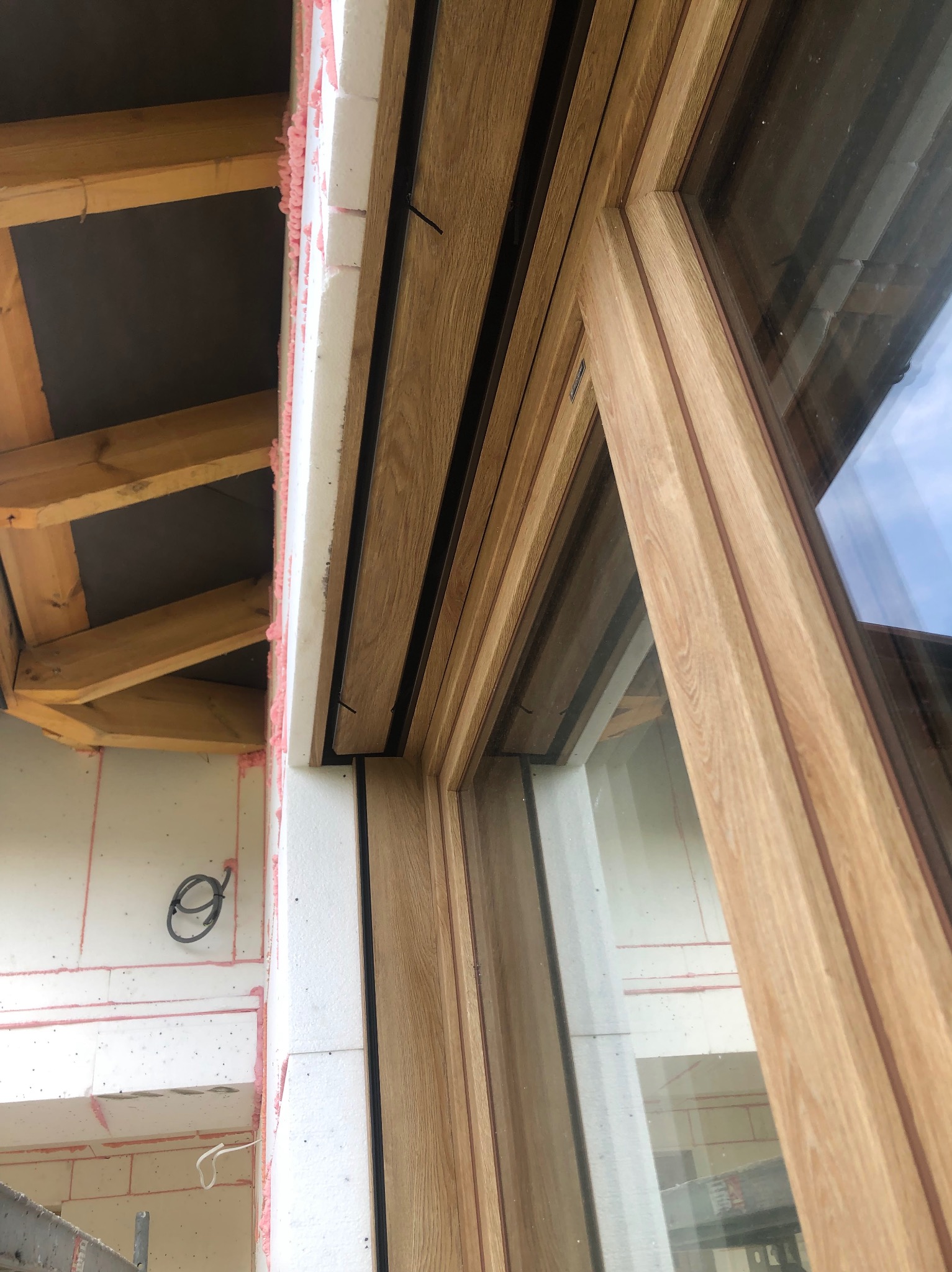 Montaż okna drewnianego z widoczną izolacją termiczną i elementami konstrukcji dachu. Ujęcie z dołu, podkreślające detale wykończenia.