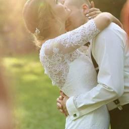 Fotografia Beata Gan - Panna młoda w koronkowej sukni i pan młody obejmują się w kontraście z promieniami słońca w tle.