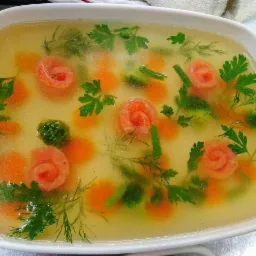 Galaretka z łososiem uformowanym w róże, marchewką, brokułami i zielenią, przygotowana w Gdańsku, w białej prostokątnej formie.