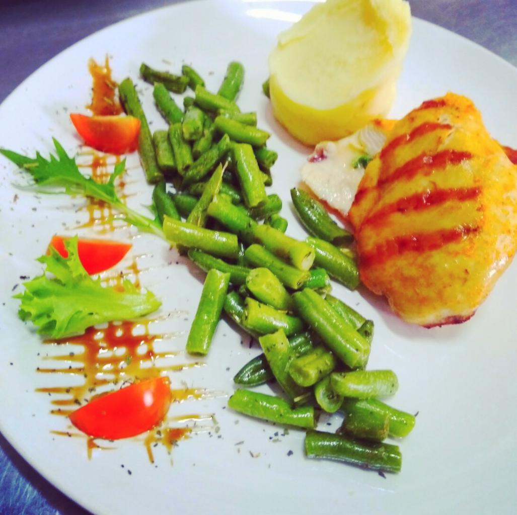 Elegancko podane danie: grillowana pierś z kurczaka z zieloną fasolką szparagową, puree ziemniaczanym, pomidorem i sosem balsamicznym na białym talerzu.