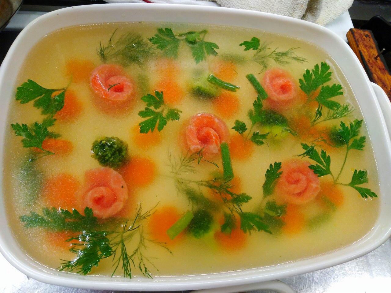 Galaretka z łososiem uformowanym w róże, marchewką, brokułami i zielenią, przygotowana w Gdańsku, w białej prostokątnej formie.