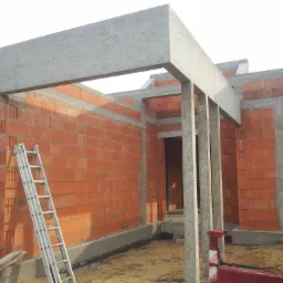 Wznoszenie ścian parterowego domu z czerwonej cegły, widoczne betonowe nadproża i słupy, drabina oparta o ścianę, surowy stan.