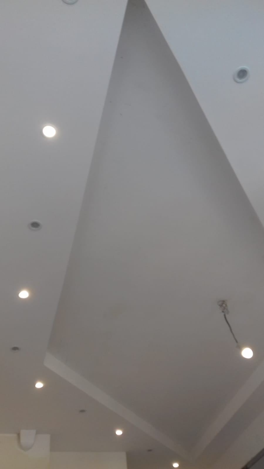 Nowoczesny biały sufit z wbudowanymi punktowymi światłami LED i dekoracyjnym podwieszanym elementem w kształcie trapezu.