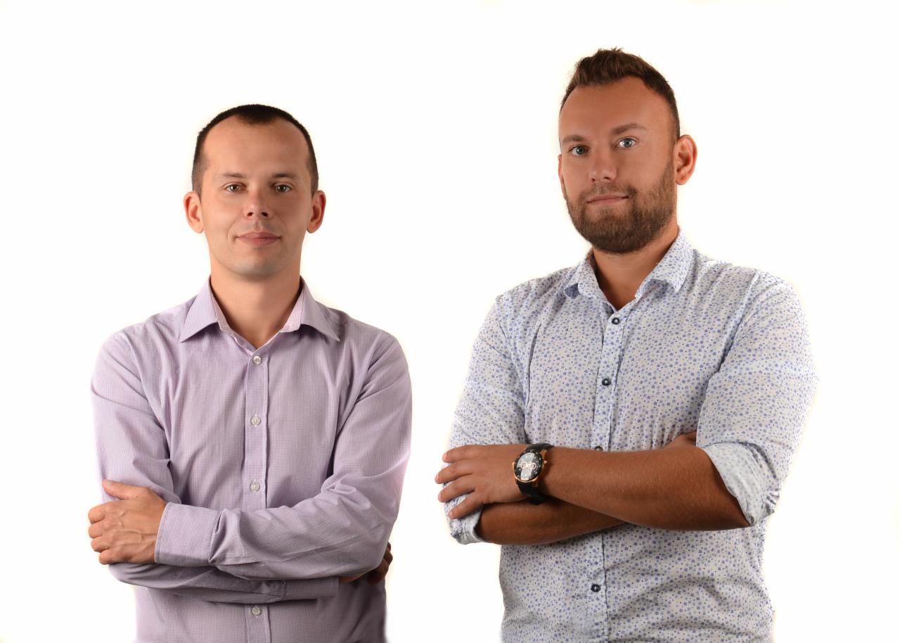 Portret dwóch mężczyzn z Krakowa w koszulach z podwiniętymi rękawami, stojących na białym tle z założonymi rękami.