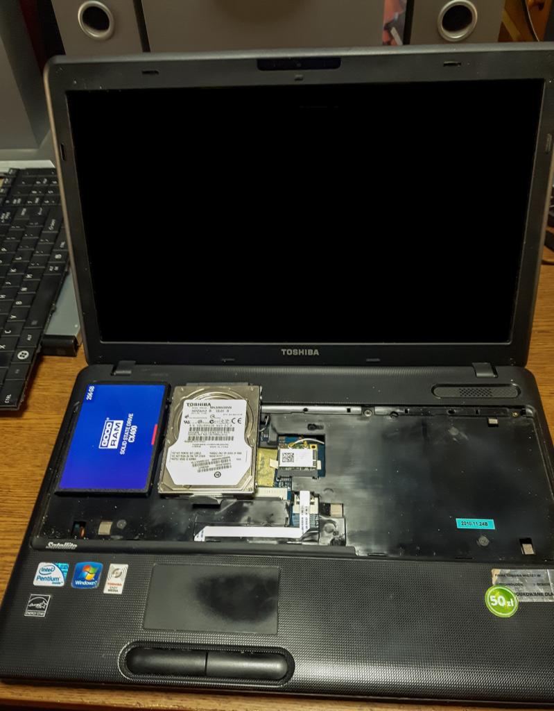 Otwarty laptop Toshiba Satellite z widocznym dyskiem twardym i modułem SSD Goodram CX400, prawdopodobnie w trakcie wymiany lub serwisu. Widoczne naklejki Intel Pentium i Windows.