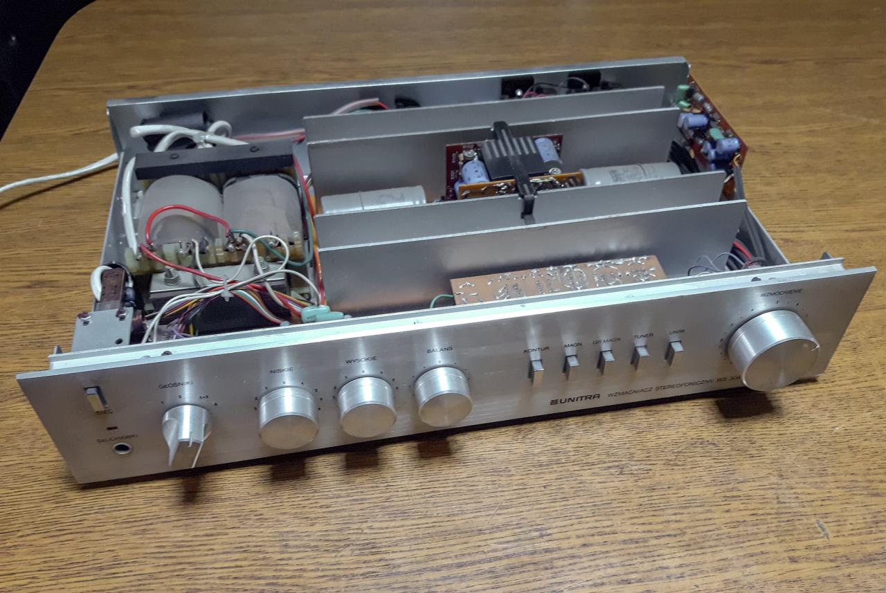 Otwarty wzmacniacz Unitra Diora WS 304 na drewnianym stole, widoczne elementy elektroniczne wewnątrz obudowy, potencjometry i przełączniki na panelu przednim.