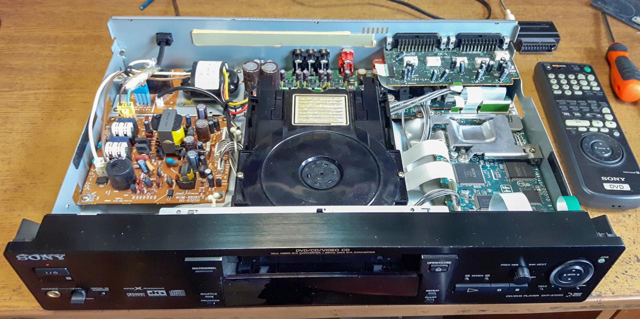 Otwarty odtwarzacz DVD Sony DVP-S725D z widocznymi płytkami drukowanymi, kondensatorami i elementami elektronicznymi, obok leży pilot i śrubokręt.