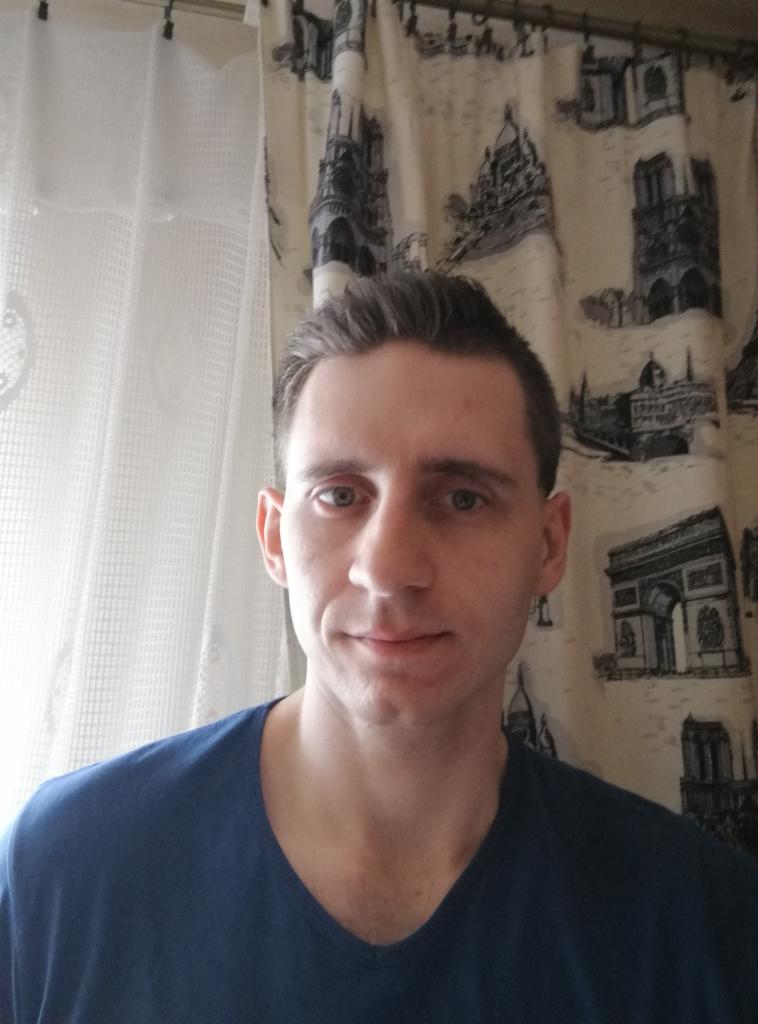 Portret mężczyzny w niebieskiej koszulce na tle zasłony z motywami architektonicznymi.