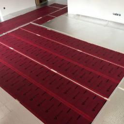 Centrum Dystrybucji ogrzewania i Fotowoltaiki Red Snake - Montaż mat grzewczych: czerwone maty z czarnym nadrukiem układane na srebrnej folii izolacyjnej, zabezpieczone taśmą, widok z góry.