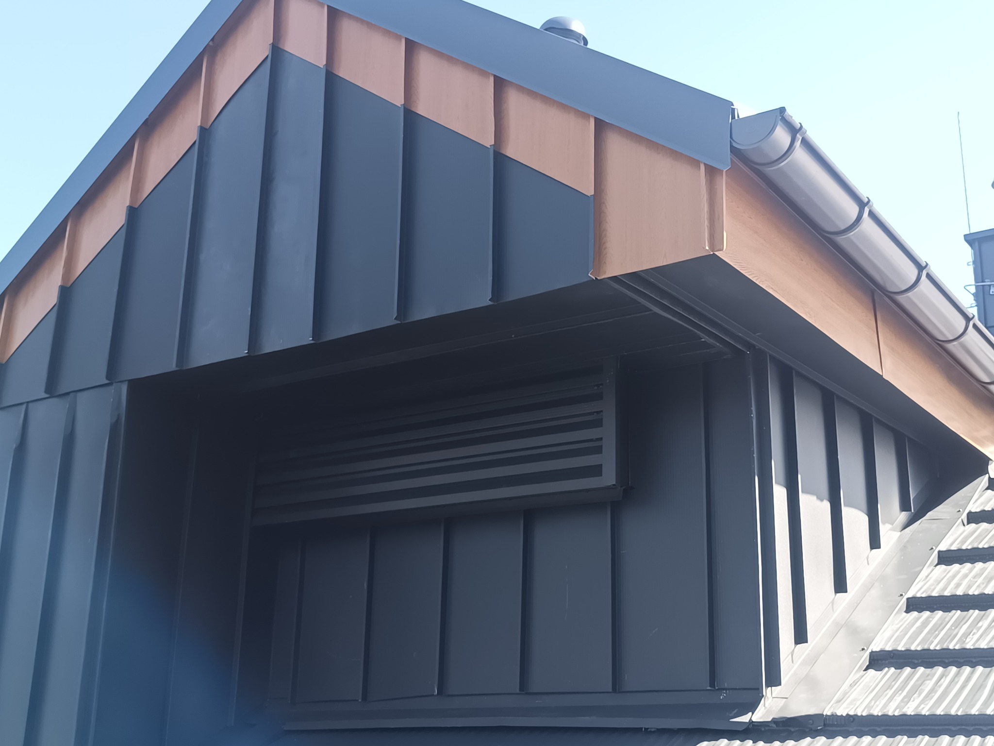 Nowoczesne wykończenie dachu z blachy w kolorze grafitowym i miedzianym. Widoczne detale obróbek blacharskich i system rynnowy w dopasowanej kolorystyce.