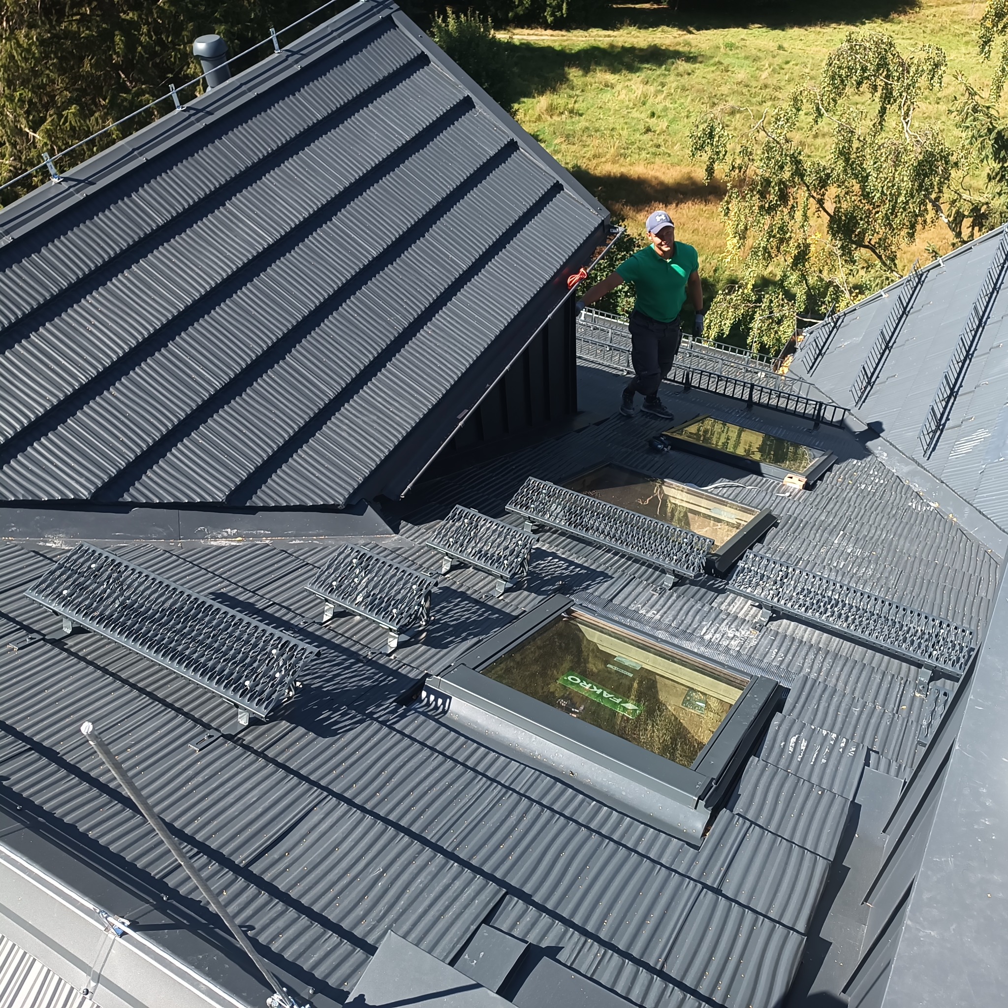 Szary dach z blachy trapezowej z oknami dachowymi i zabezpieczeniami. Prace dekarskie w Kotli. Widoczny dekarz przy krawędzi dachu.