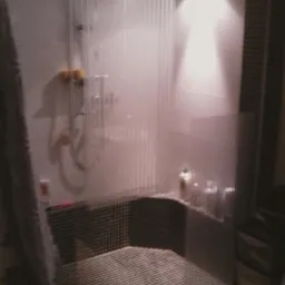 Wykończona kabina prysznicowa z mozaiką, widok z boku, z widocznymi akcesoriami łazienkowymi na półce i zasłoną prysznicową z tworzywa.