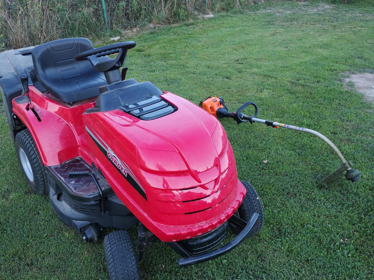 Czerwony traktorek do koszenia trawy z kosiarką żyłkową leżącą obok na trawniku.