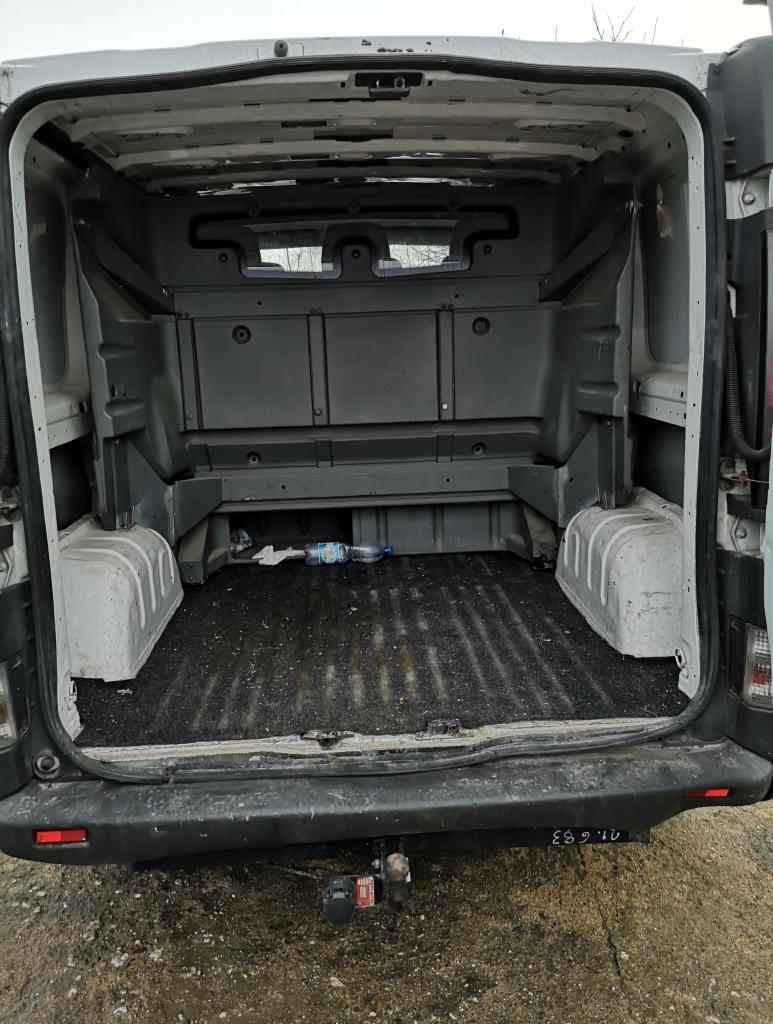 Wnętrze paki brudnego busa transportowego, widok z tyłu, z butelką wody i papierami na podłodze.