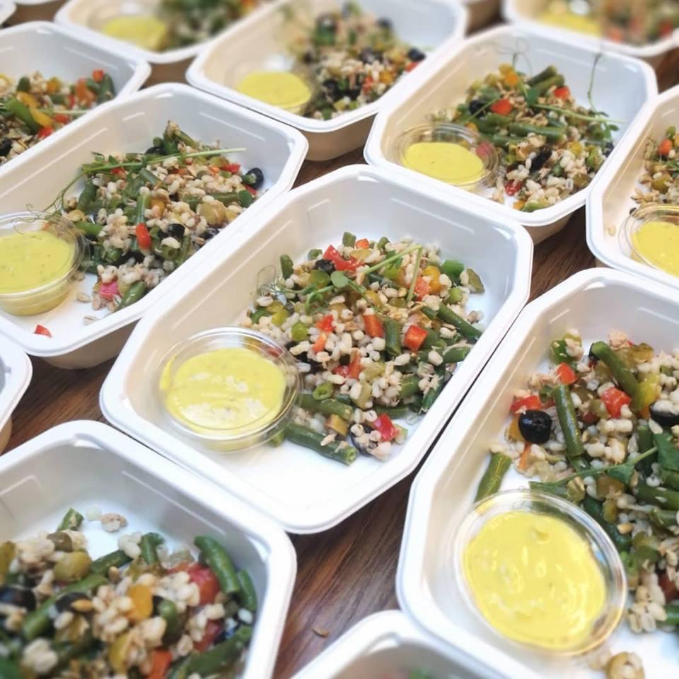 Porcje sałatki z kaszą, zieloną fasolką, papryką i oliwkami w białych pojemnikach z sosem na drewnianym stole, przygotowane do cateringu dietetycznego.