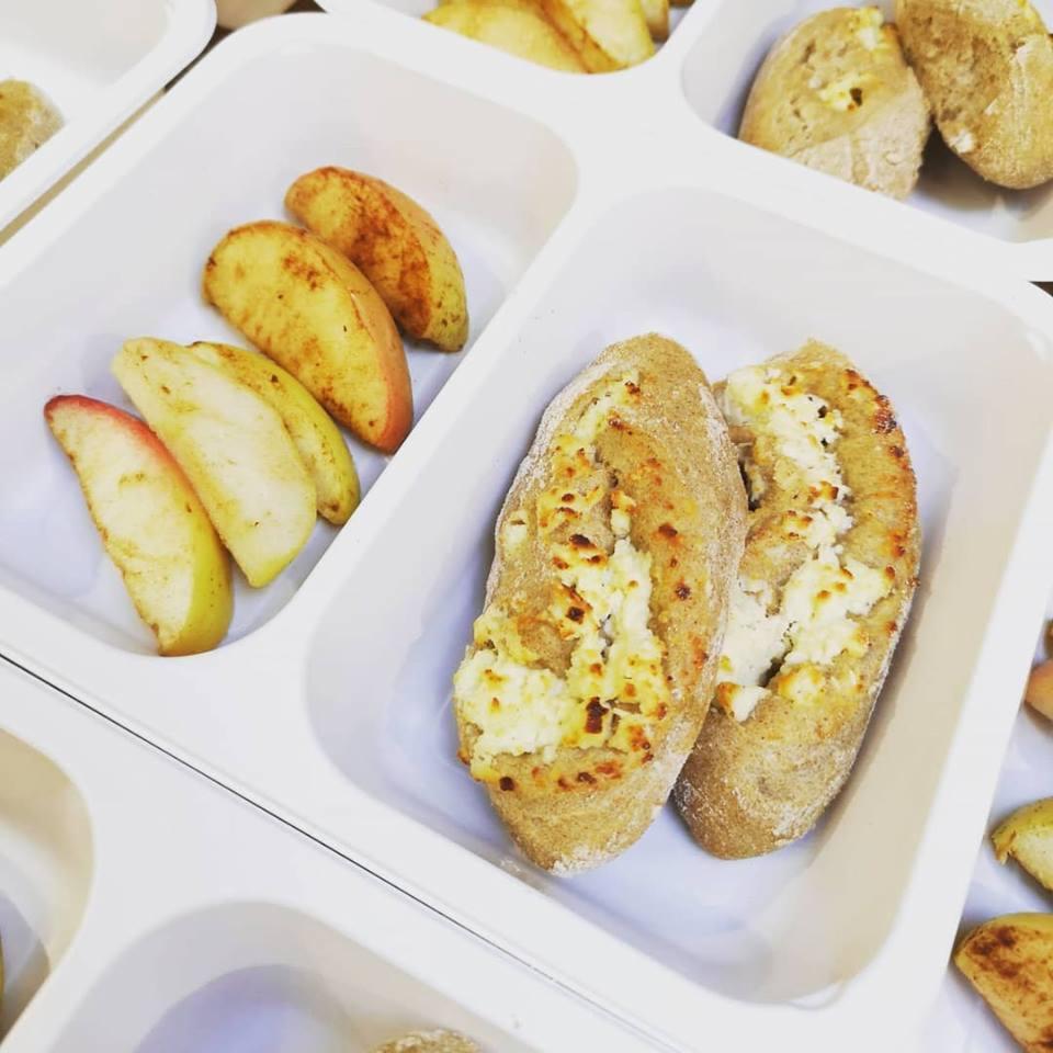 Biała tacka z dwoma przegródkami zawierającymi: w jednej pieczone kromki chleba z serem, a w drugiej cząstki pieczonych jabłek z czerwoną skórką, element posiłku dietetycznego.