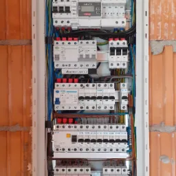 Rozdzielnica elektryczna z zainstalowanym smart miernikiem Fronius i zabezpieczeniami Eaton, zamontowana na ścianie z cegły ceramicznej dziurawki.