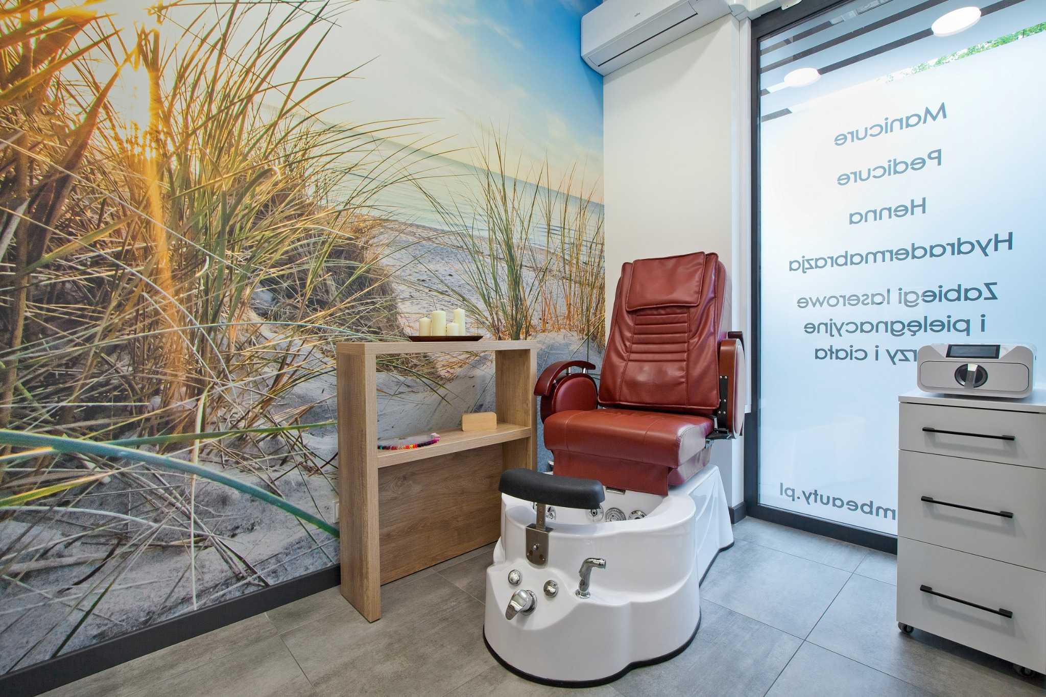 Nowoczesne wnętrze salonu z fotelem do pedicure, tłem z motywem plaży i minimalistyczną półką z dekoracjami, tworzące relaksującą atmosferę.