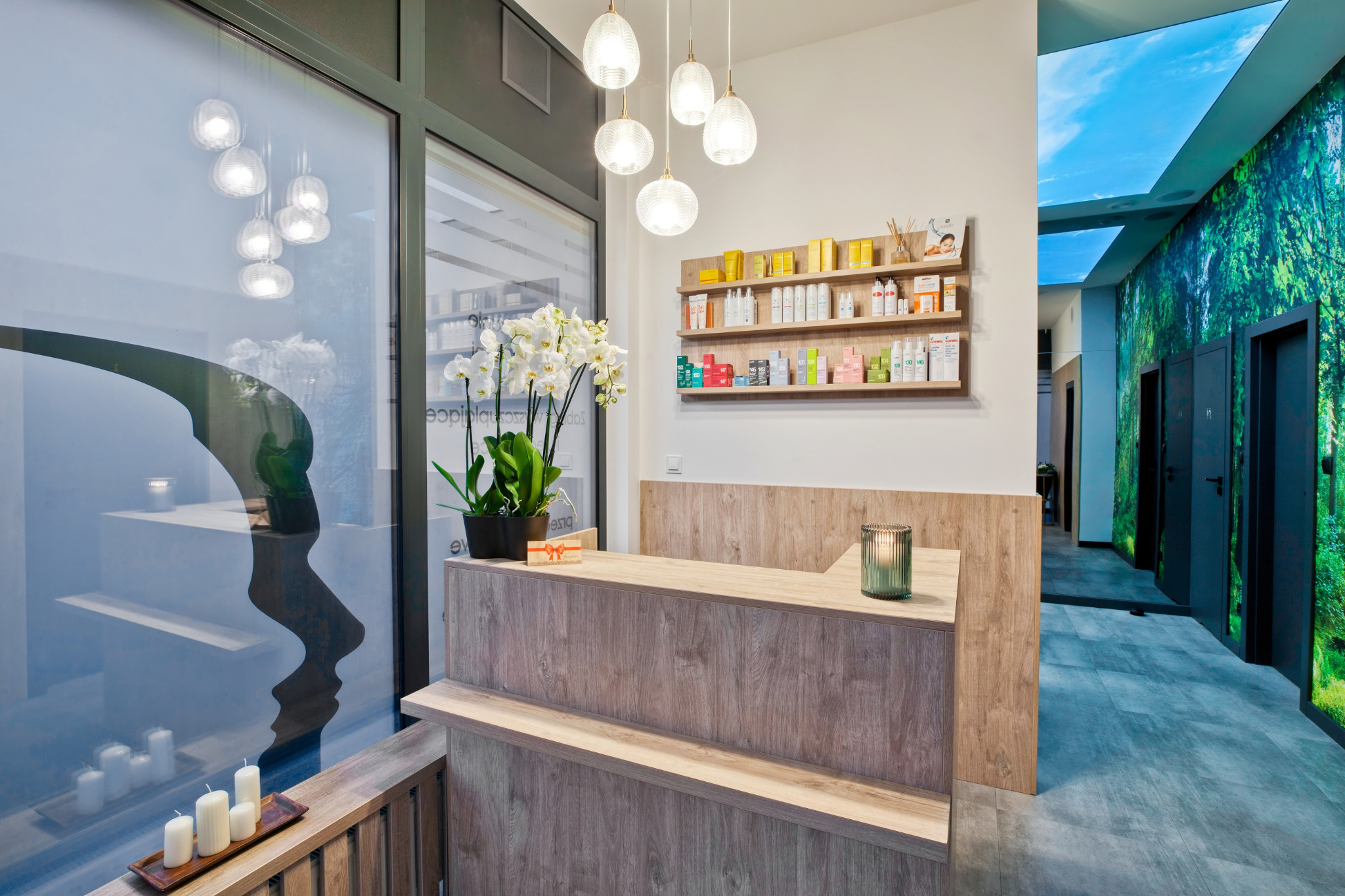 Recepcja w nowoczesnym salonie z drewnianym wykończeniem, dekorowana białymi storczykami w czarnej doniczce, świecami i szklaną ozdobą, na ścianie półki z kosmetykami, w tle fototapeta z motywem...