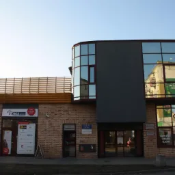 Budynek usługowy z biurem Fines oferującym kredyty, widoczny szyld 'Tutaj otrzymasz kredyt', ceglana fasada, okna z reklamami i refleksami innych budynków.