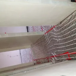 Montaż ogrzewania podłogowego w budynku w Cycowie: białe rurki układane na siatce, widok z g&oacute;ry na sufit i instalację.