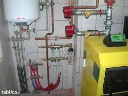 Kotłownia z żółtym piecem, instalacją hydrauliczną z miedzianymi rurami, zbiornikiem na wodę i rozdzielaczem podłogówki, widok z boku.