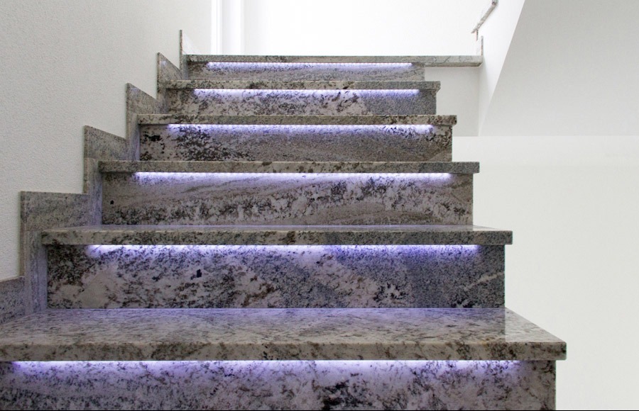 Granitowe schody wewnętrzne z subtelnym, fioletowym podświetleniem LED pod każdym stopniem, ukazane z dołu.