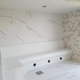 Wykończona łaźnia parowa z mozaikową ławką i płytkami imitującymi marmur na ścianach oraz geometrycznym wzorem na jednej ze ścian.