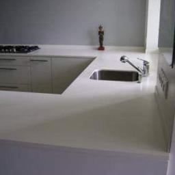 db BEAUTY - Biały blat kuchenny z wbudowanym zlewem i płytą grzewczą, minimalistyczny styl, dekoracyjna figurka na blacie w tle.