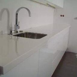 db BEAUTY - Biały blat kuchenny z wbudowanym zlewem i chromowaną baterią, minimalistyczny design, widoczne niedokończone prace wykończeniowe na ścianie.